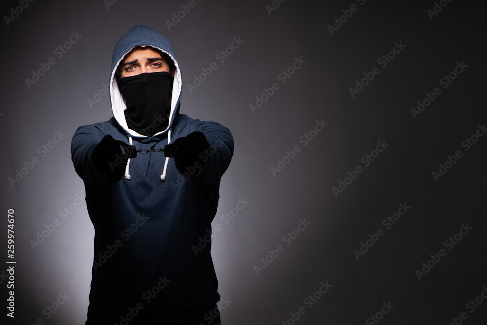 Young gangster in hood on grey background 