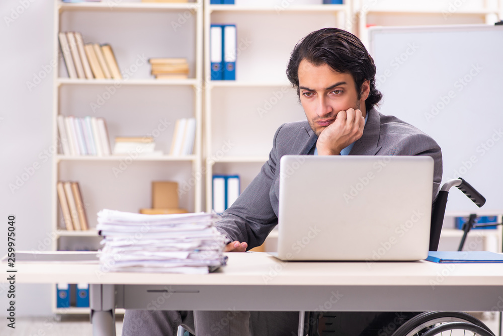 Young handsome employee in wheelchair at the office Young handsome employee in wheelchair at the office