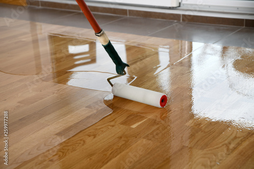 Lacquering wood floors. Worker uses a roller to coating floors.
