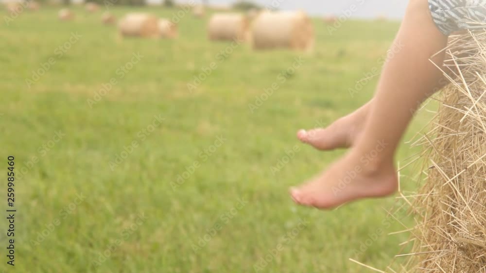 Boy sitting on stack of hay in summer dangling his bare feet Boy sitting on stack of hay in summer dangling his bare feet