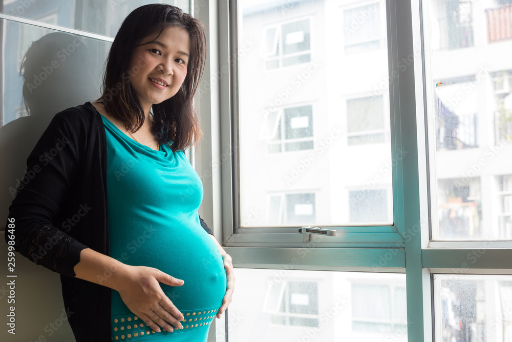 Beautiful happy asian pregnant women standing in room by window