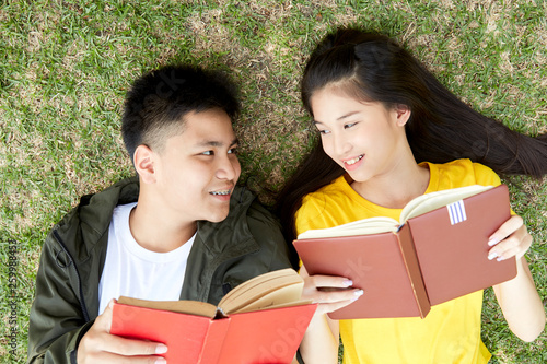 Teenagers with books lying on green grass