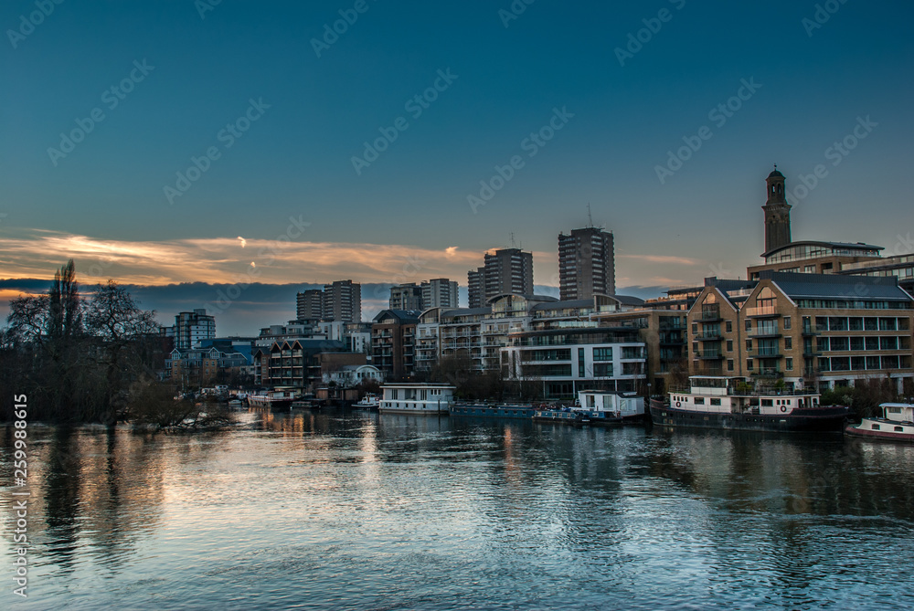 Boats and apartment buildings are reflected in the  River Thames