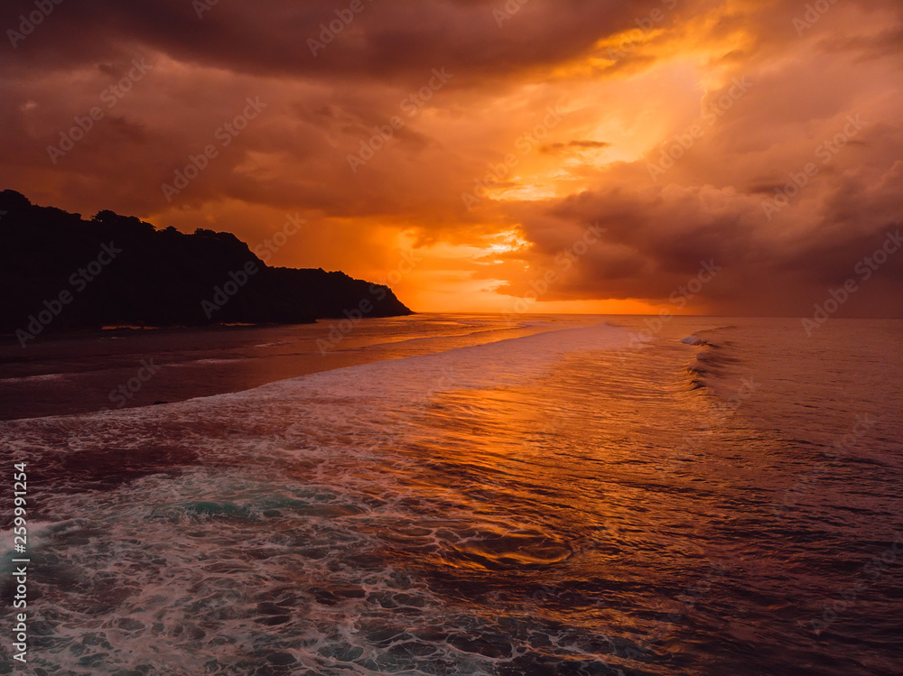 Aerial view of ocean with waves and warm sunset or sunrise.