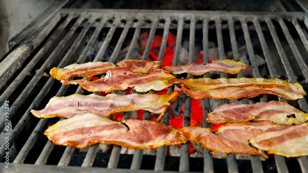 Eight slices of bacon lie on the roasted grill reach their readiness, braised coals and light smoke