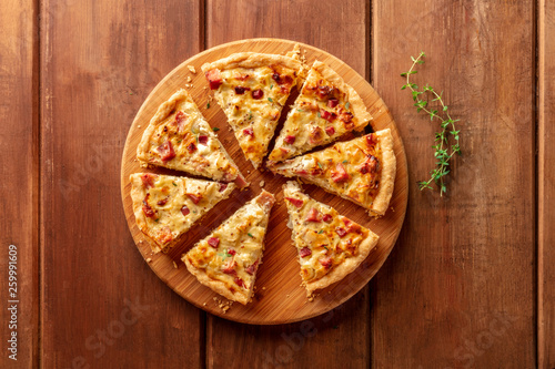 A photo of a quiche with thyme, shot from the top on a dark rustic wooden background with a place for text