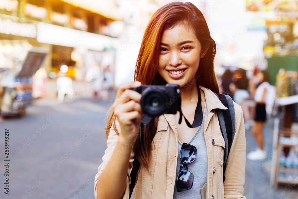 Young Asian female tourist woman with smile holding a camera and taking photos in Bangkok, Thailand while travelling in Southeast Asia