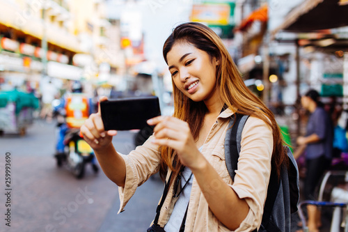 Young Asian female tourist woman taking selfie photos with smartphone while travelling in Bangkok, Thailand