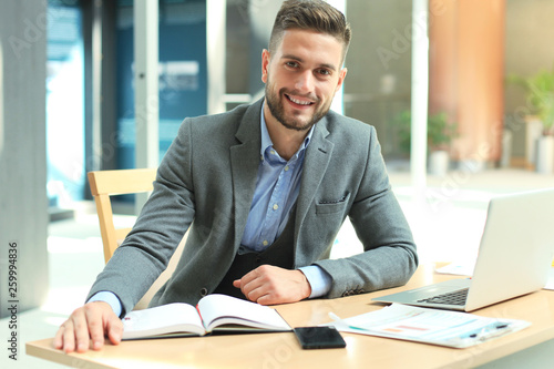 Foto Portrait of happy businessman sitting at office desk, looking at camera, smiling