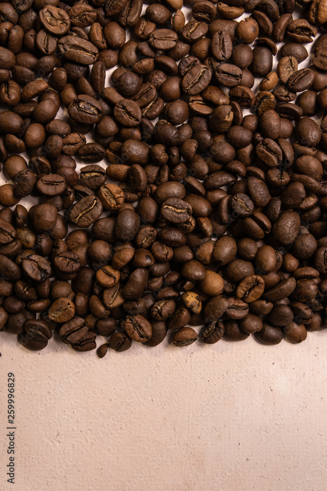 Fototapeta premium Roasted coffee beans in bulk on a light pink background. dark cofee roasted grain flavor aroma cafe, natural coffe shop background, top view from above, copy space