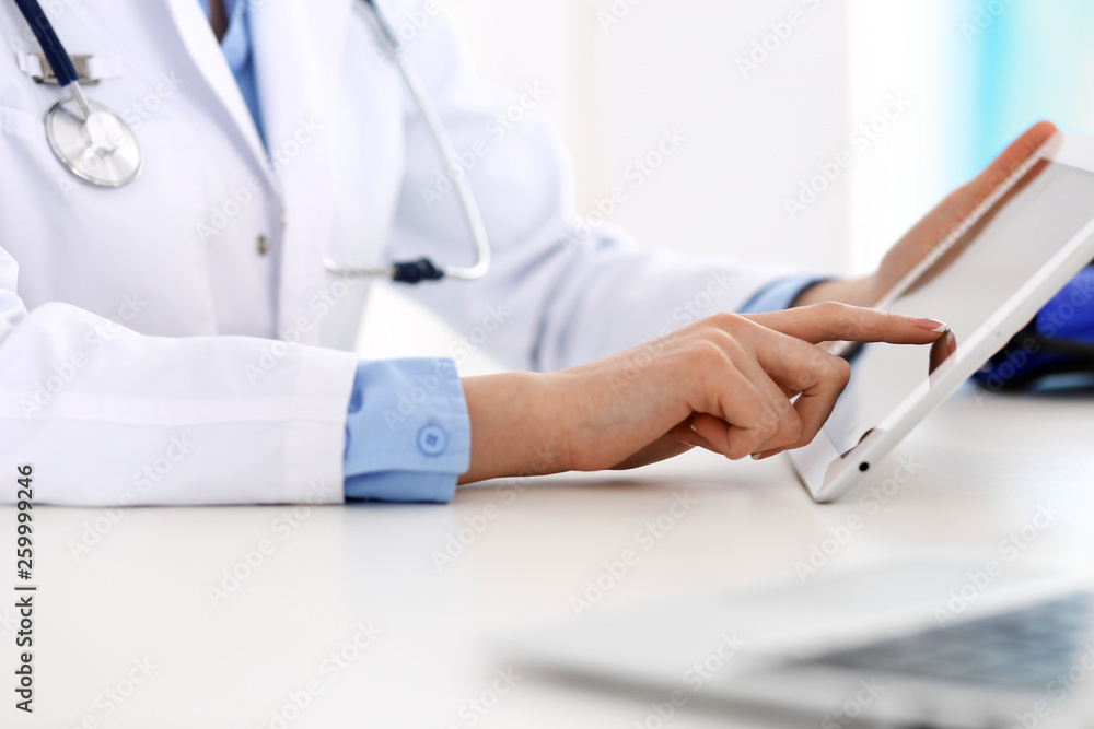 Doctor working table. Woman physician using tablet computer while sitting in hospital office close-up. Healthcare, insurance and medicine concept
