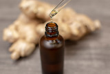 ginger oil dropping in brown bottle with blurred ginger root on background