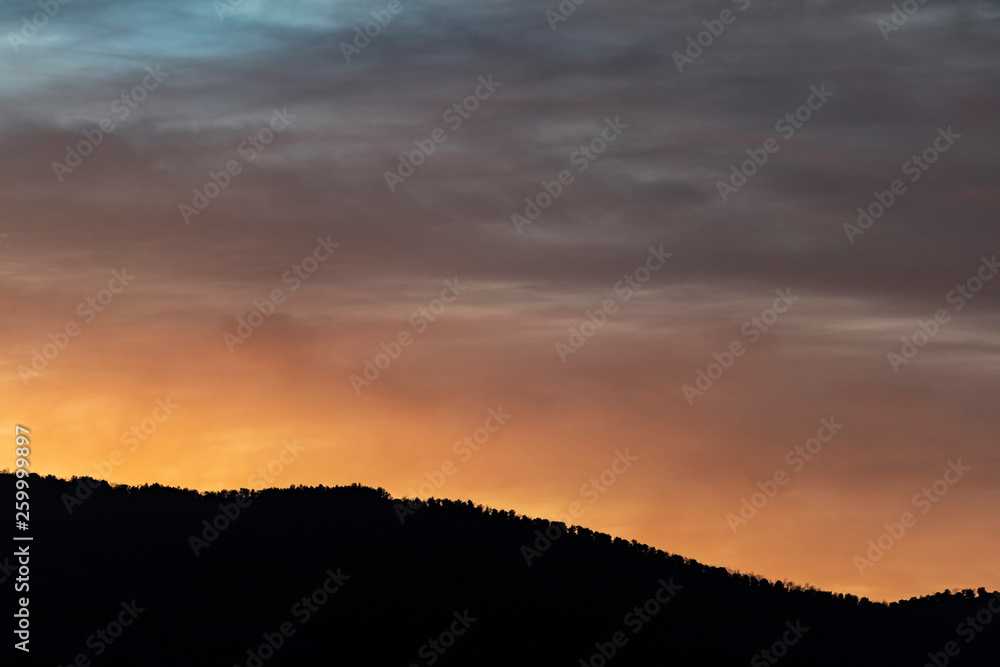 Orange cloudy sunset with mountain silhouette Orange cloudy sunset with mountain silhouette