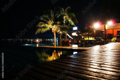 Night view of palm trees reflected in the pool, located on the beach