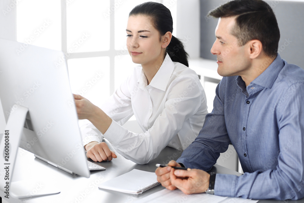 Cheerful smiling businessman and woman working with computer in modern office. Headshot at meeting or workplace. Teamwork, partnership and business concept Cheerful smiling businessman and woman working with computer in modern office. Headshot at meeting or workplace. Teamwork, partnership and business concept