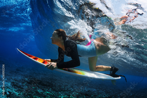 Underwater shot of the young woman surfer diving under the wave with her surfboard