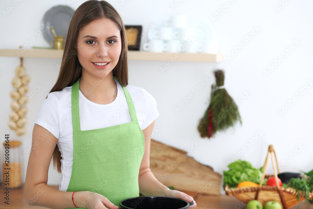 Young happy woman cooking soup in the kitchen. Healthy meal, lifestyle and culinary concept. Smiling student girl preparing vegetarian meal at home