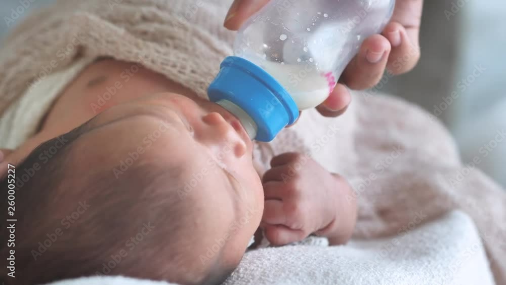 Asian female newborn baby lying in bed and Suck milk Bottle in home with sunlight in the morning. Cute little girl three weeks old.  hungry, Crying, wriggle, emotion concept