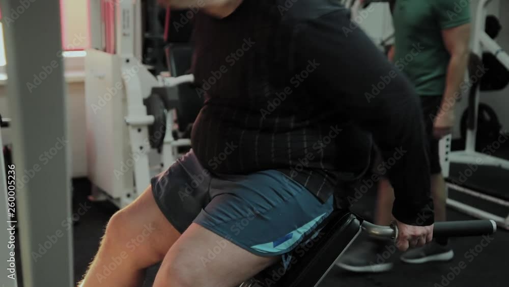 Cheerful fat man performs a wrong exercise in the gym. For the first time in a fitness club. Cheerful fat man performs a wrong exercise in the gym. For the first time in a fitness club.