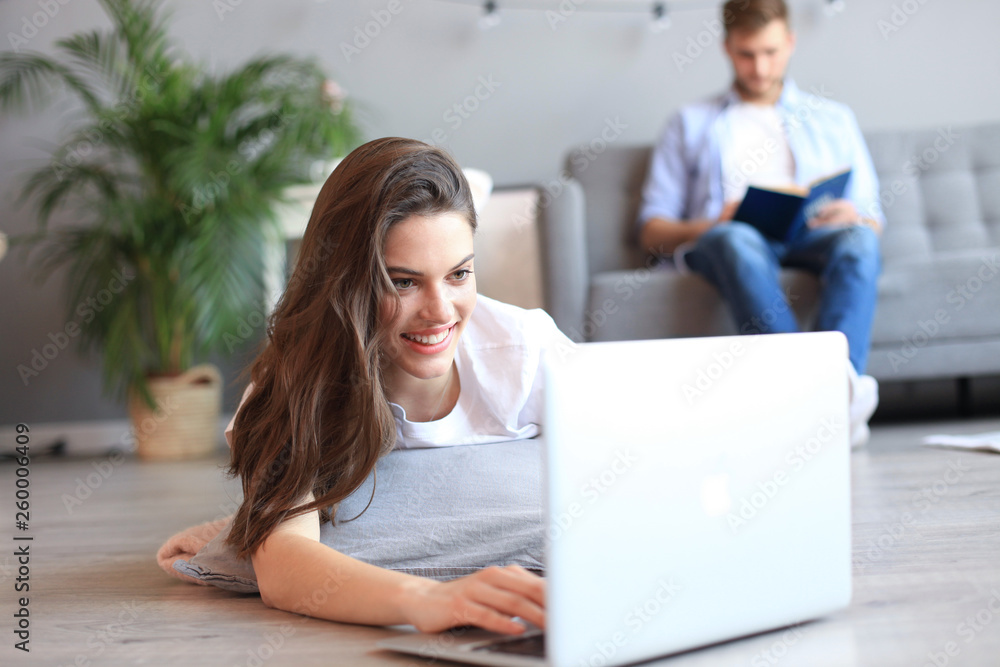 Fototapeta premium Smiling beautiful woman using laptop with blurred man in background at home.