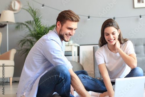 Young couple doing some online shopping at home  using a laptop on floor.