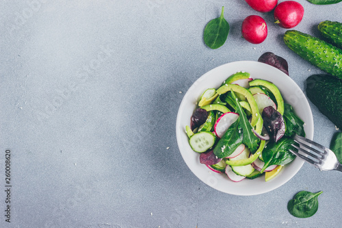 Healthy salad with radishes, avacado, cucumbers, spinach and arugula in a bowl top view