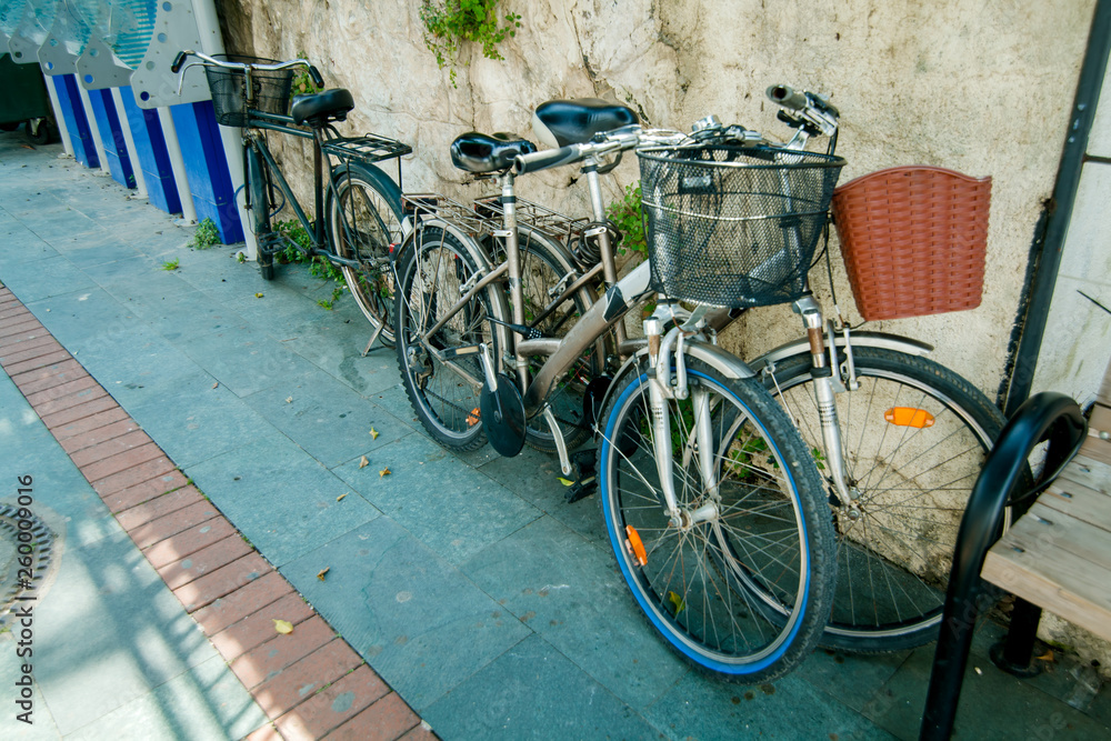 bicycles are available for rent with food baskets on the street along the stone wall on the sidewalk