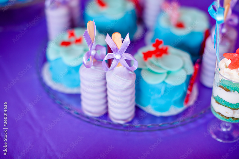Birthday party concept. Table for kids with cupcakes with blue and red top and decored items in bright blue and purple colors. Summer season delicious on the party. Sea time theme on the candy bar