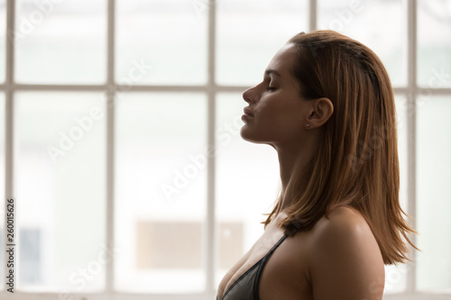 Portrait of beautiful woman meditating with closed eyes, practicing yoga