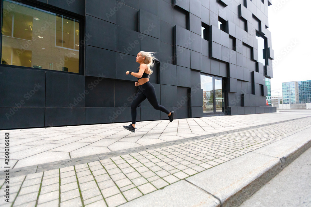 Fototapeta premium Fast running young woman wearing sports top in modern city environment