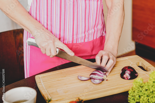 Female hands cutting bulb Edelweiss onionon wooden board, in kitchen. photo