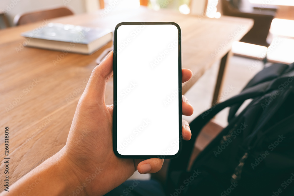 Mockup image of a man's hand holding and showing black mobile phone with blank white screen while sitting in cafe