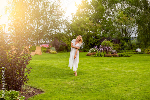 Youmg beautiful blond woman in beautiful summer garden is barefoot on lawn photo