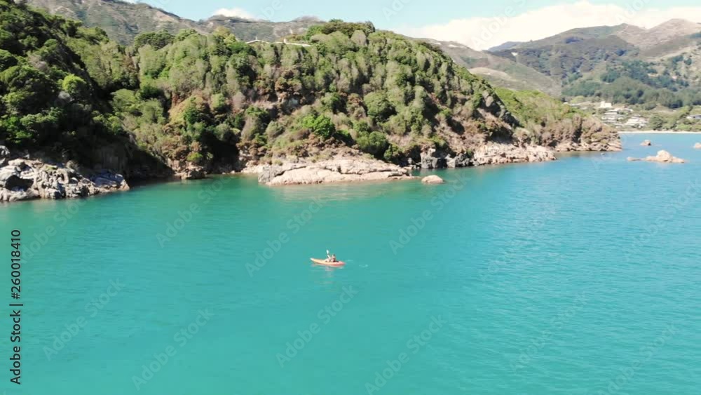 Drone flying over a man whose kayaking near stunning New Zealand tropical coastline in Abel Tasman National Park with tropical blue oceans, beautiful sand bars, coastal forests and jagged rocks. Drone flying over a man whose kayaking near stunning New Zealand tropical coastline in Abel Tasman National Park with tropical blue oceans, beautiful sand bars, coastal forests and jagged rocks.
