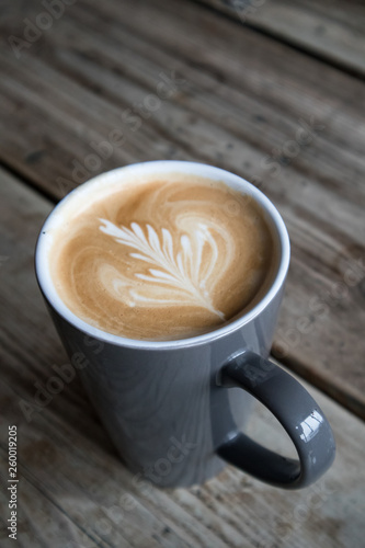 Coffee in cup with leaf design created with milk on the top with rustic blurred wooden background
