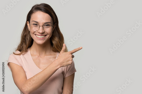 Friendly woman in glasses pointing finger to copyspace studio shot