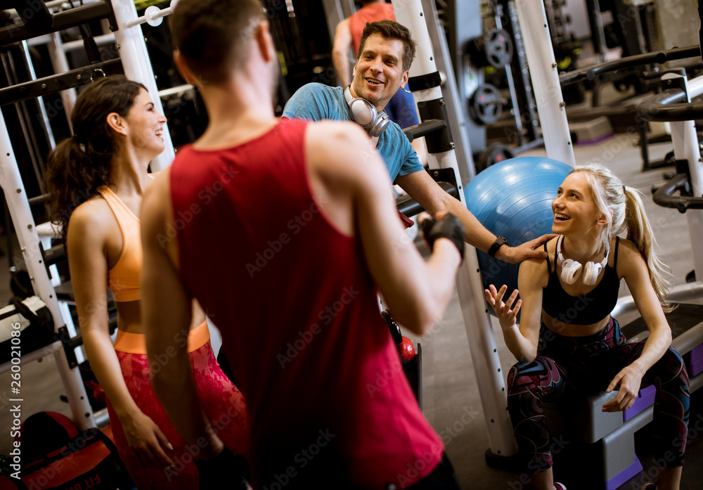 Group of young friends talking and laughing while sitting together on the floor of gym after  workout
