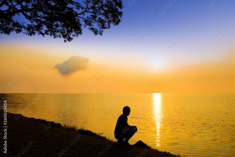 Man in silhouette squatting under the sunrise peacefully looking out to the ocean