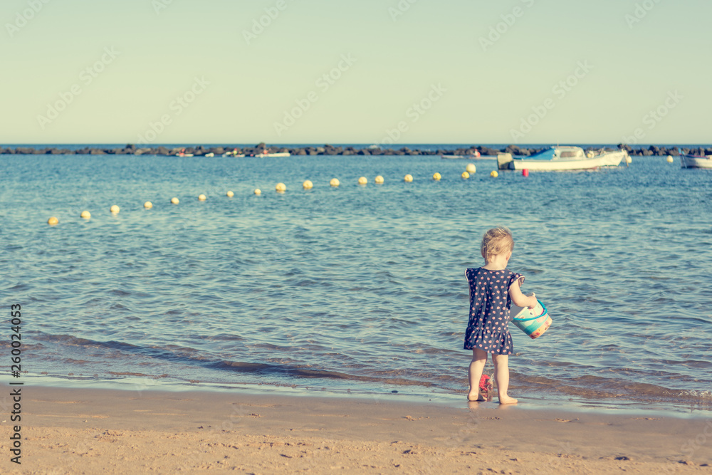 Cute little girl playing on sandy beach and exploring.