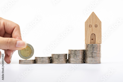 Woman's hand putting coin on coins stacks with house model. Concept for property ladder, mortgage and real estate investment . photo