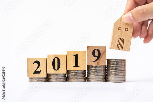 Woman's hand putting house model on coins stack and 2019 wooden block. Concept for property ladder, mortgage and real estate investment . photo