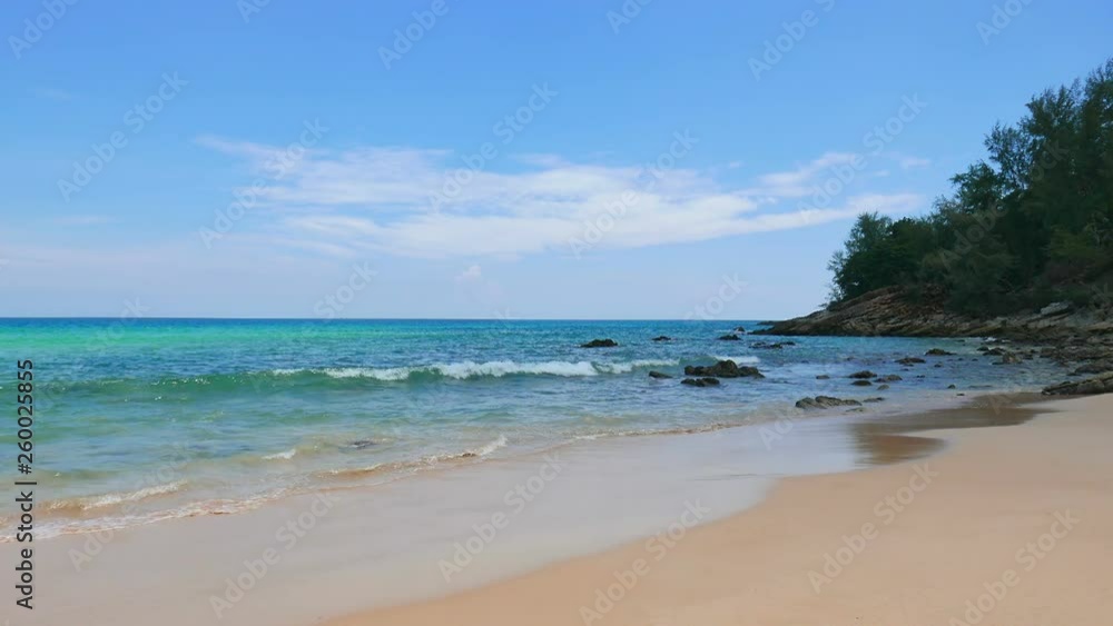 Turquoise water sea wave breaking on shore in tropical beach with rocks and hill on blue sky background at daytime Turquoise water sea wave breaking on shore in tropical beach with rocks and hill on blue sky background at daytime