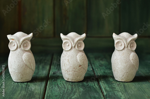 Three figurines of owls standing in a row on a green wooden background