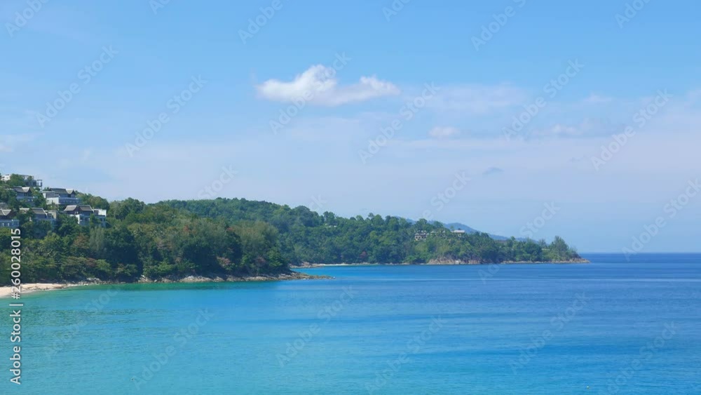 Peaceful turquoise blue water sea near island shore with forest hill and little town on blue sky at daytime Peaceful turquoise blue water sea near island shore with forest hill and little town on blue sky at daytime