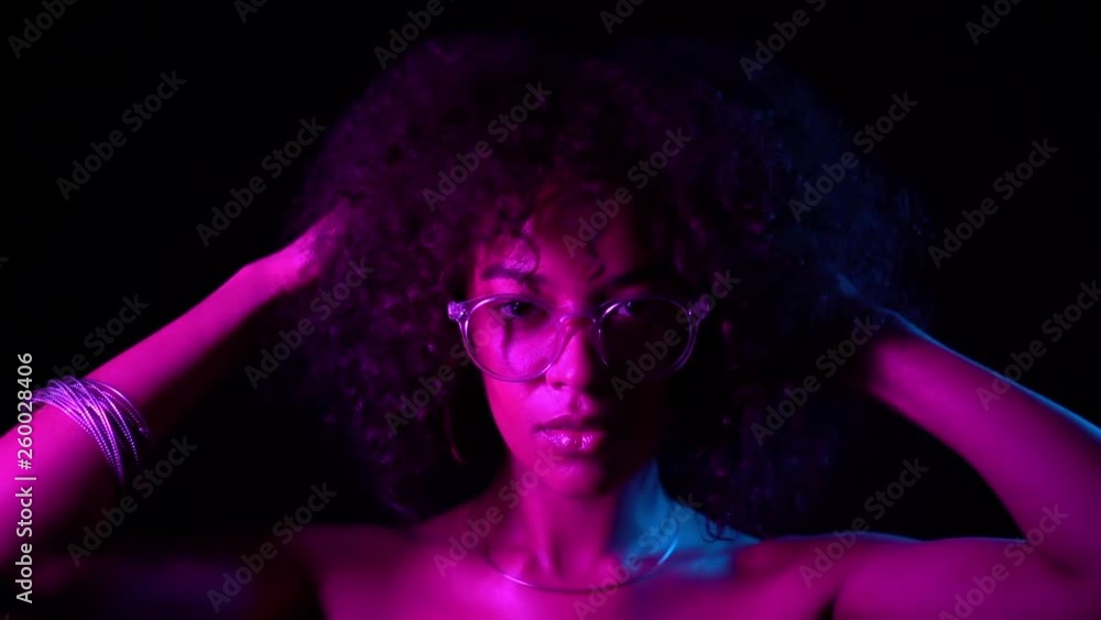 Tempting woman with perfect make-up and transparent glasses posing in dark room at night. Portrait of young sexy african girl in neon light Tempting woman with perfect make-up and transparent glasses posing in dark room at night. Portrait of young sexy african girl in neon light