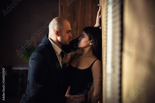 A bald man in a black suit pressed a beautiful dark-haired girl against the wall, the girl holding on to a tie. Horizontal photography