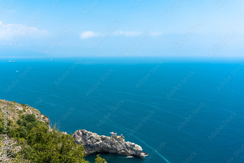 View of the beautiful blue sea from a cliff, Amalfi Coast. Visible bay and ruins of a small castle on the cliff. Ships are sailing in the distance