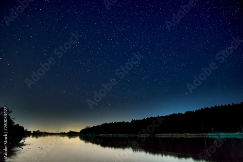 Wonderful beautiful night sky full of stars with Milky way over the river and forest in transparent april night