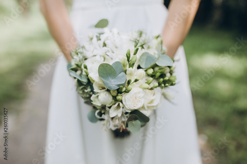 bride in white dress holding a wedding bouquet of flowers and greenery