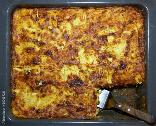 Closeup fresh cooked in the oven traditional Greek homemade food of pasticcio (pastitsio) in a black baking pan cut in servings and a spatula photo